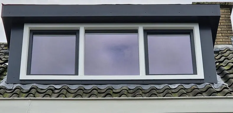 Dakkapel met antraciet bekleding en een wit kozijn met drie ramen, waarvan twee met een antraciet vleugel.