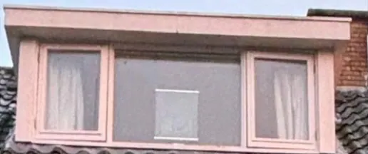 Dezelfde dakkapel vóór de renovatie, met verkleurde kozijnen en een verkleurde dakrand.