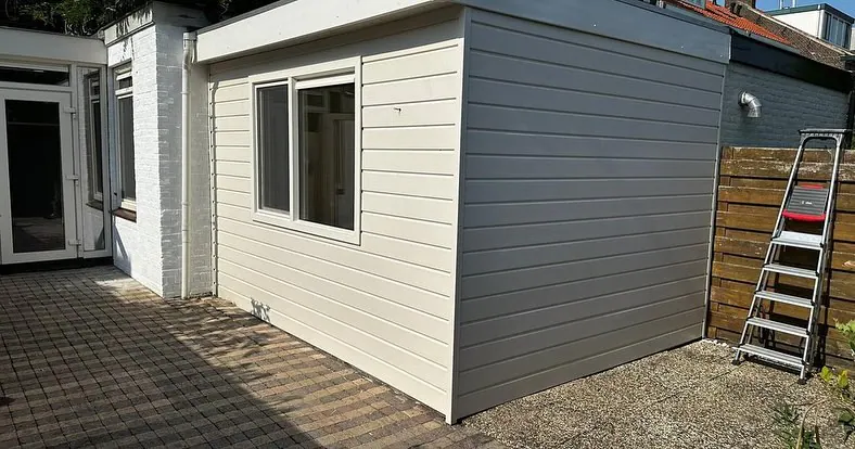 Aanbouw met lichte gevelbekleding en een kozijn in dezelfde kleur, met links de tuindeuren.