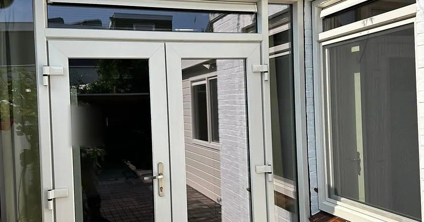 Dubbele tuindeuren in een lichte kleur met een bovenlicht en glas aan weerszijden.