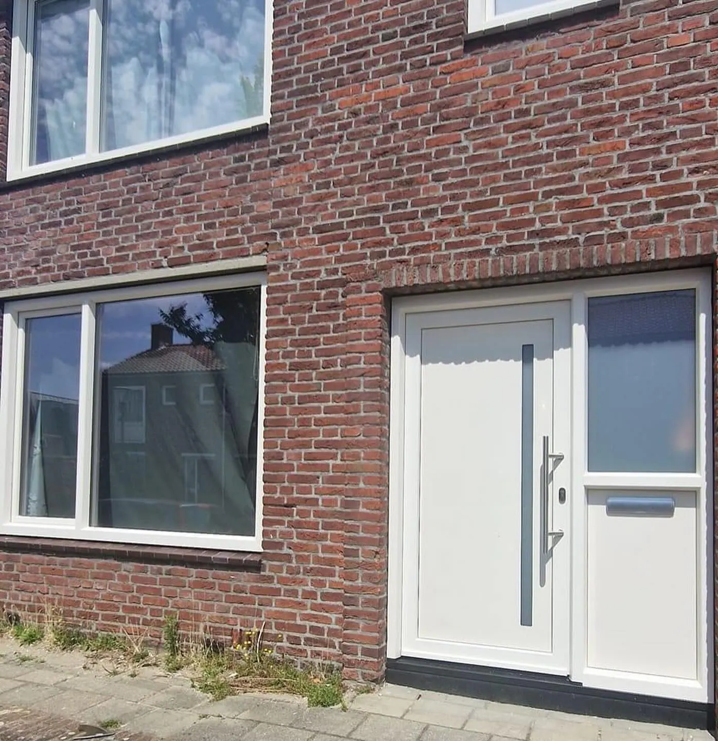 Witte voordeur met een smalle glasstrook en een zijlicht met matglas, naast een wit kozijn in een rode bakstenen gevel.